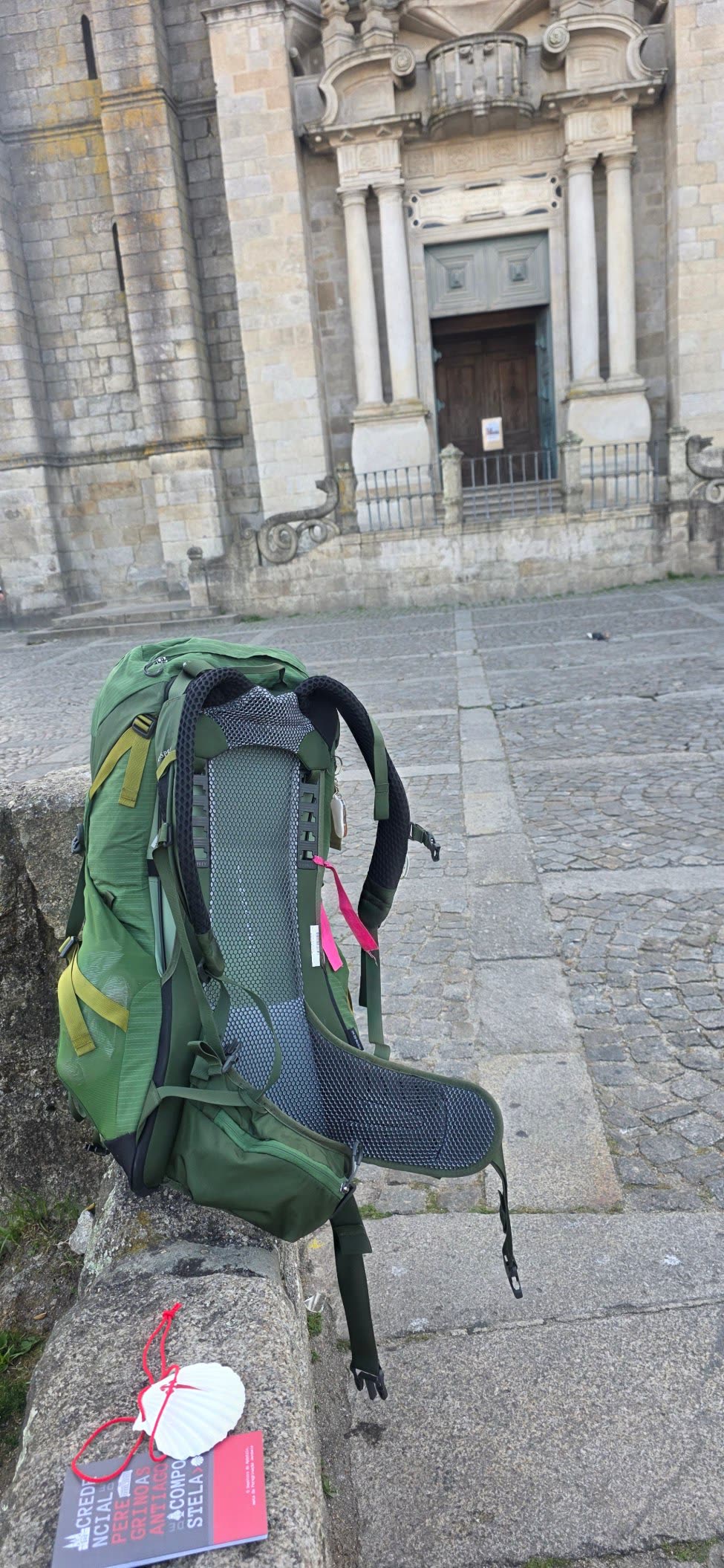 Green backpack, scallop shell and credencial resting before a stone church