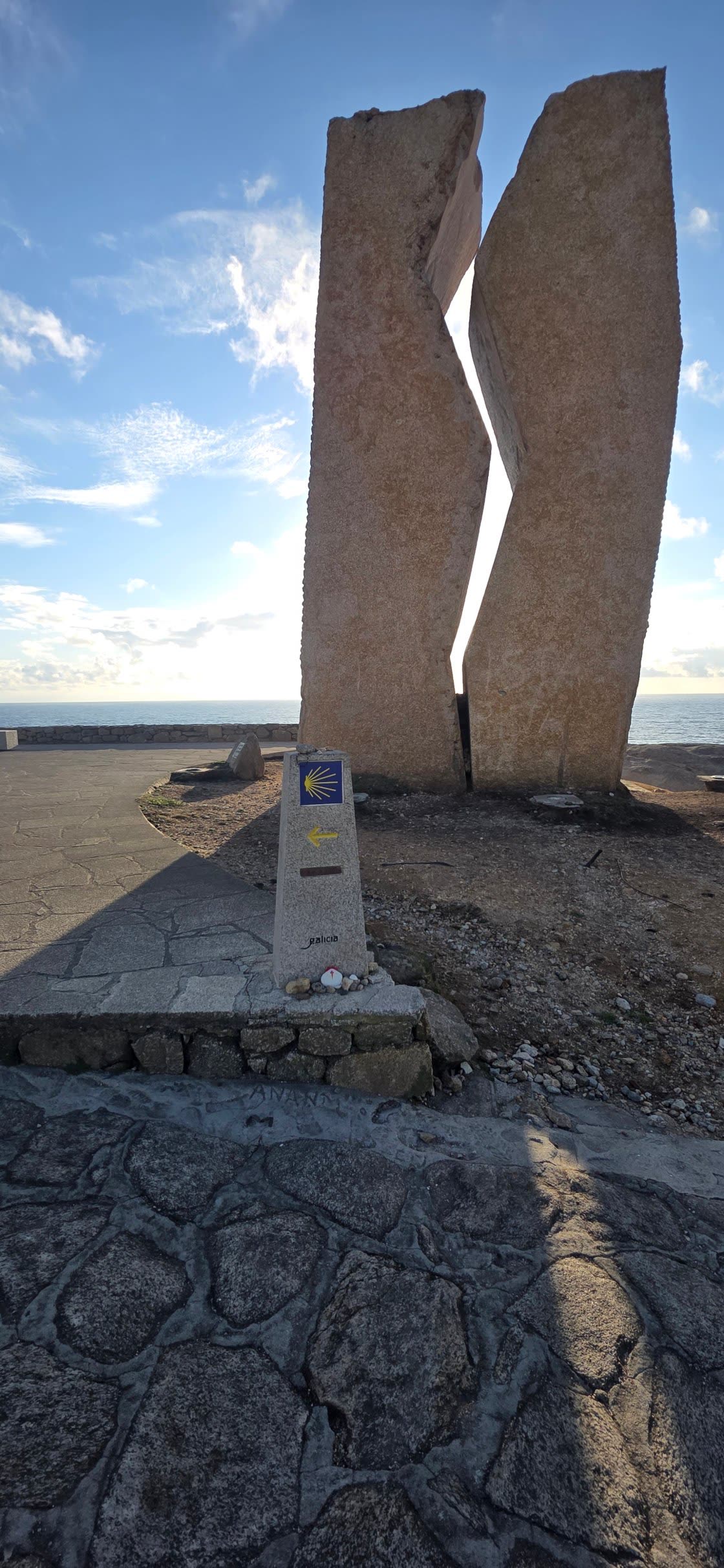Split rock monument by the sea with a Camino waymarker